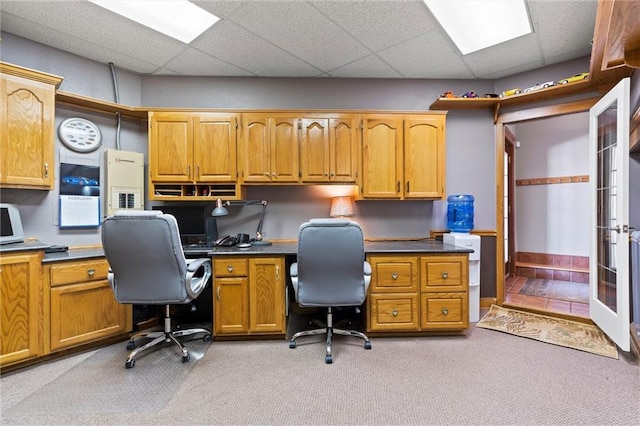 office space featuring a paneled ceiling, light carpet, and built in study area