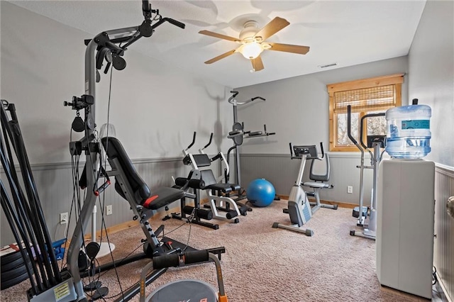 exercise room with ceiling fan, visible vents, carpet flooring, and wainscoting