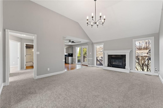 unfurnished living room with baseboards, a premium fireplace, carpet flooring, ceiling fan with notable chandelier, and high vaulted ceiling