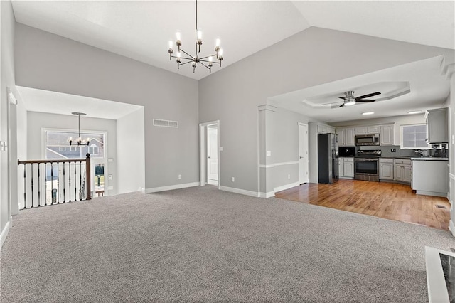 unfurnished living room featuring visible vents, baseboards, light carpet, ceiling fan with notable chandelier, and high vaulted ceiling