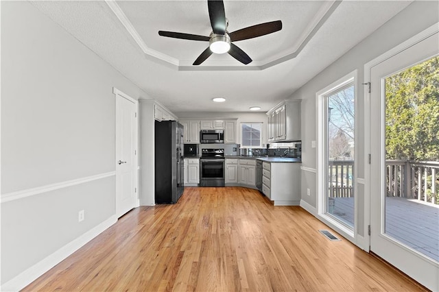 kitchen featuring visible vents, light wood-style flooring, a tray ceiling, stainless steel appliances, and baseboards