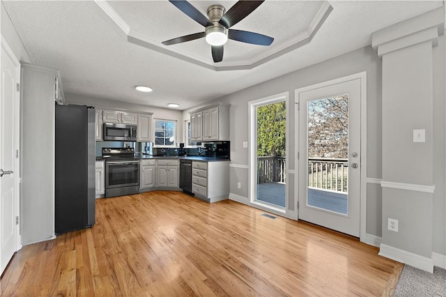 kitchen featuring visible vents, gray cabinetry, a tray ceiling, dark countertops, and appliances with stainless steel finishes