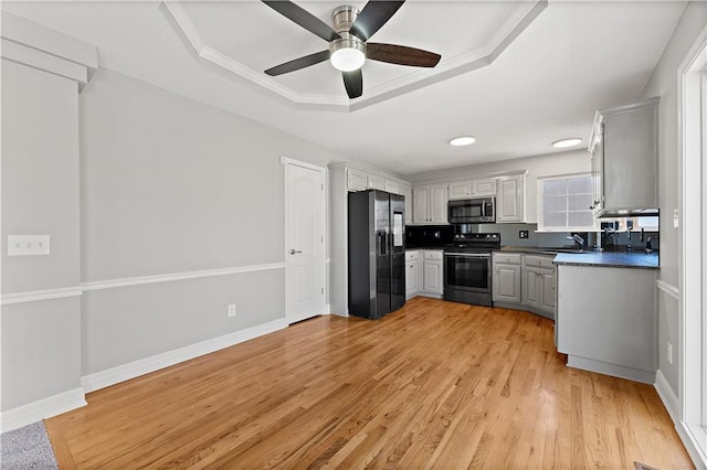 kitchen with dark countertops, appliances with stainless steel finishes, light wood-style floors, a raised ceiling, and a sink