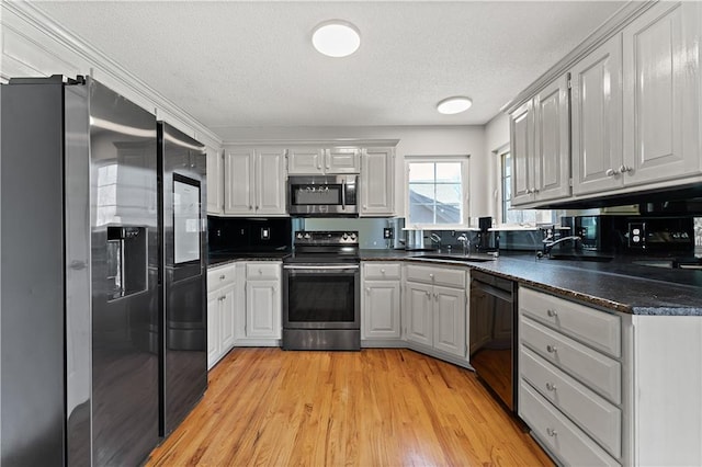 kitchen with dark countertops, light wood-type flooring, stainless steel appliances, a textured ceiling, and a sink