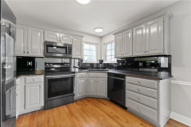 kitchen with dark countertops, light wood-type flooring, stainless steel appliances, a textured ceiling, and a sink