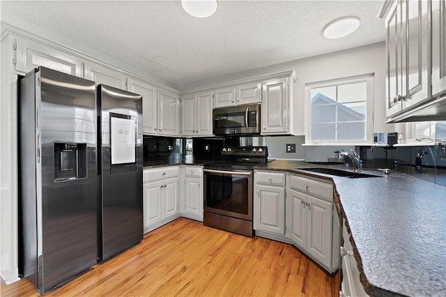 kitchen featuring a sink, light wood-style floors, appliances with stainless steel finishes, a textured ceiling, and dark countertops