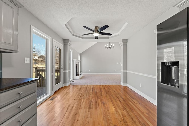 interior space with visible vents, a fireplace with raised hearth, a tray ceiling, light wood-style floors, and a textured ceiling