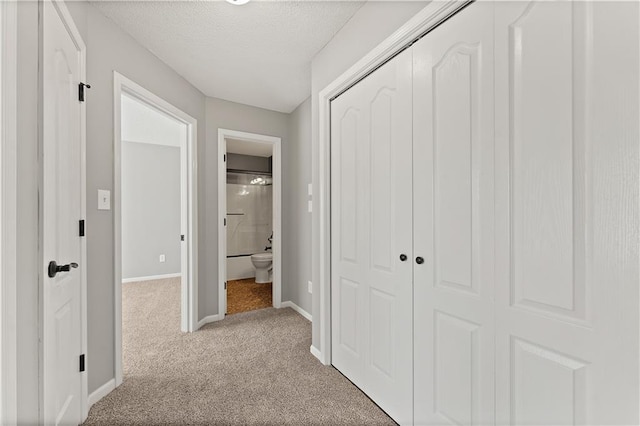 corridor featuring carpet flooring, baseboards, and a textured ceiling