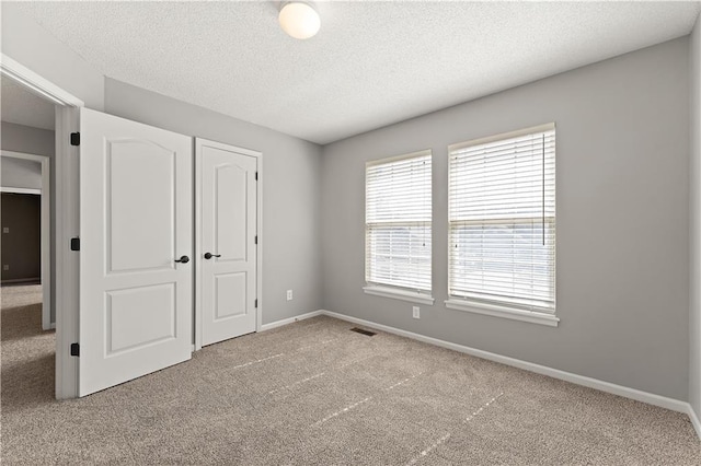 unfurnished bedroom with baseboards, carpet floors, a textured ceiling, and visible vents