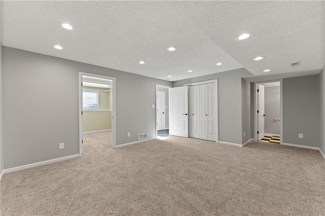 interior space with visible vents, light colored carpet, a textured ceiling, and baseboards