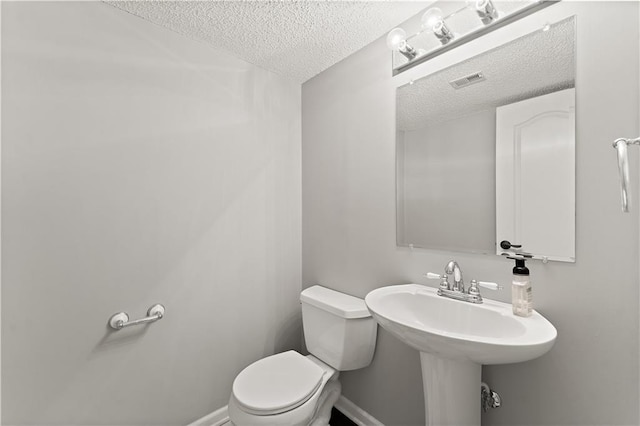 bathroom featuring toilet, baseboards, visible vents, and a textured ceiling