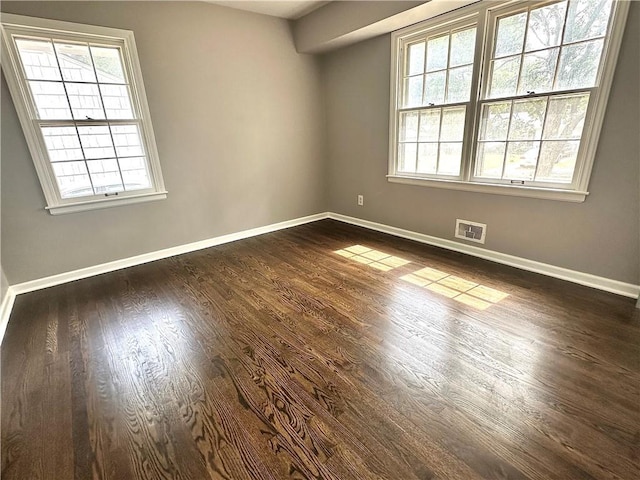 spare room featuring baseboards, dark wood-style floors, visible vents, and a healthy amount of sunlight