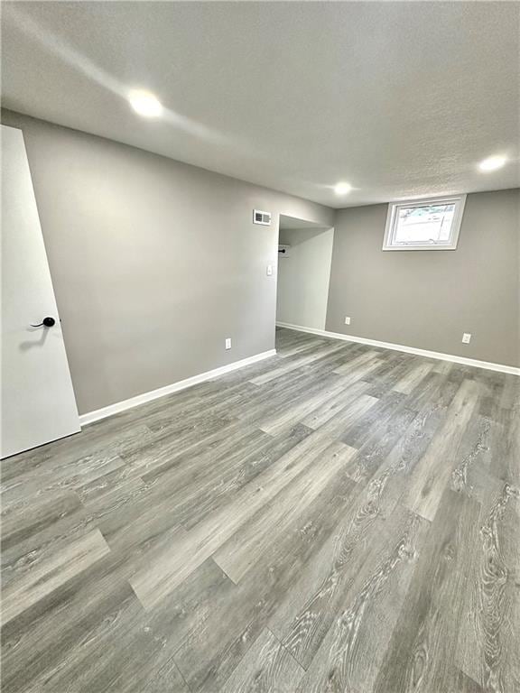 basement with visible vents, a textured ceiling, baseboards, and wood finished floors