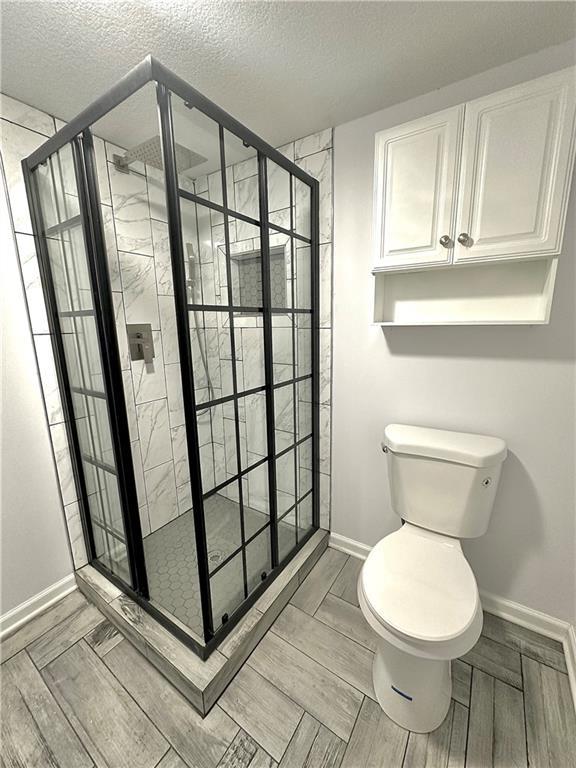 bathroom featuring a stall shower, toilet, a textured ceiling, and baseboards