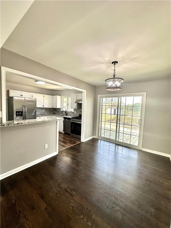 kitchen with a peninsula, white cabinetry, appliances with stainless steel finishes, dark wood-style floors, and tasteful backsplash