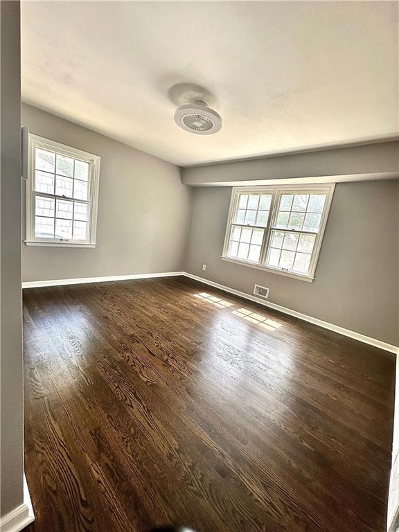 unfurnished room featuring visible vents, baseboards, and dark wood finished floors