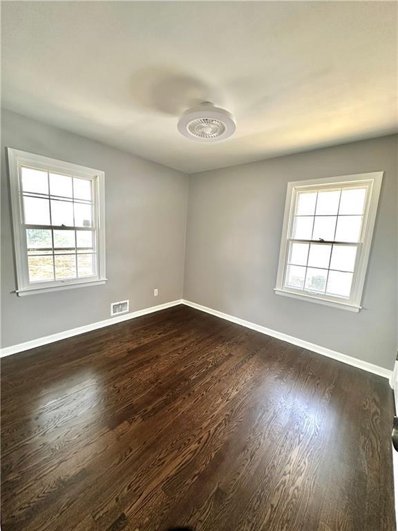 spare room with dark wood finished floors, visible vents, and baseboards