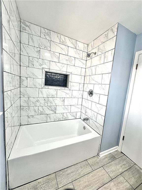 full bathroom featuring baseboards, wood finish floors, and shower / bathing tub combination