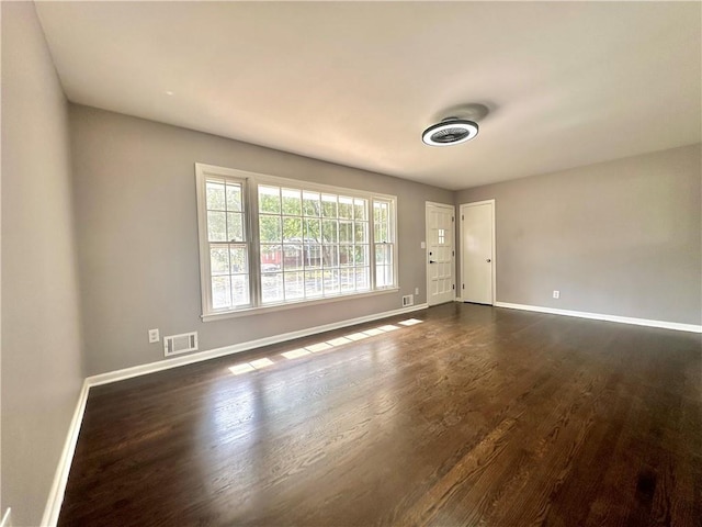 unfurnished room featuring dark wood-style floors, visible vents, and baseboards