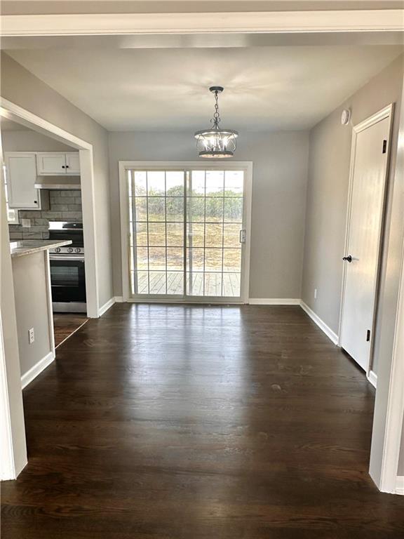 unfurnished dining area featuring dark wood-style floors, a notable chandelier, and baseboards