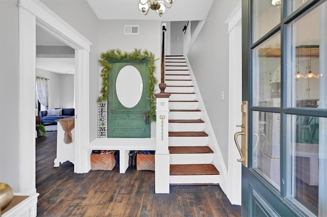 foyer entrance featuring stairs, dark wood finished floors, visible vents, and a notable chandelier