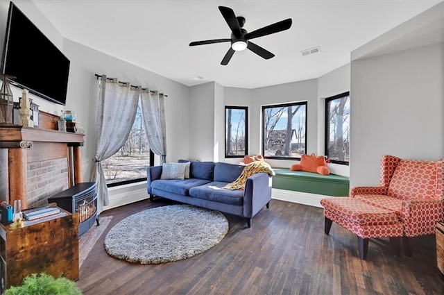 living room with a wood stove, visible vents, ceiling fan, and wood finished floors