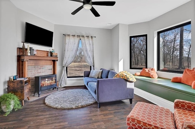 living room featuring a ceiling fan, wood finished floors, a wood stove, and baseboards