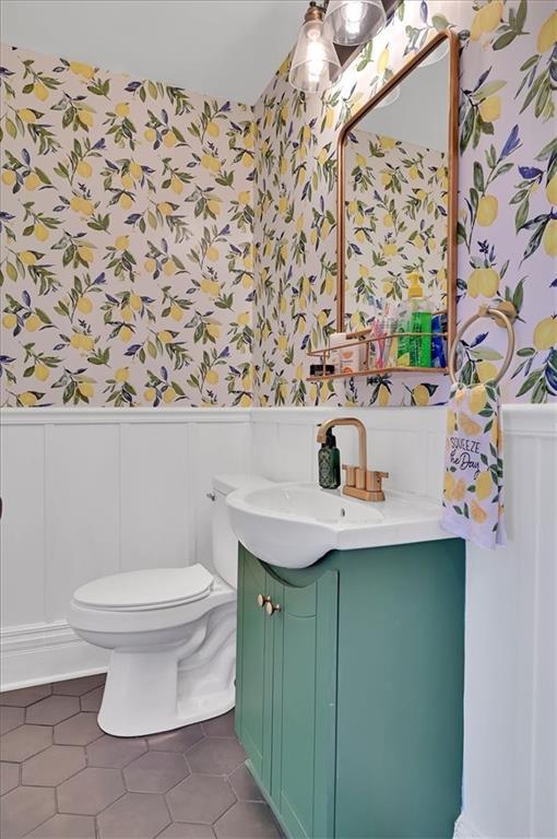 bathroom with wallpapered walls, wainscoting, toilet, tile patterned floors, and vanity