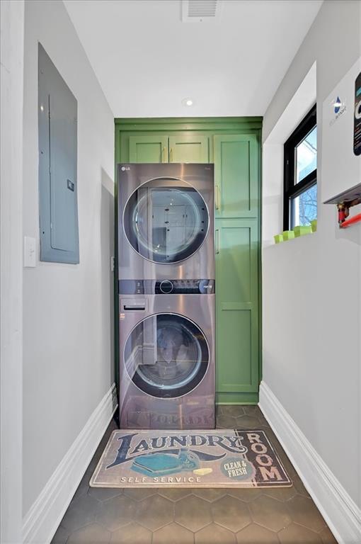 laundry area with cabinet space, electric panel, baseboards, and stacked washer and clothes dryer