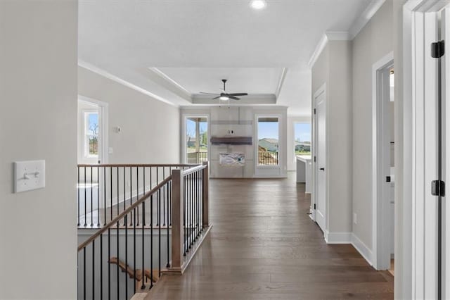 hall featuring baseboards, ornamental molding, a tray ceiling, and an upstairs landing