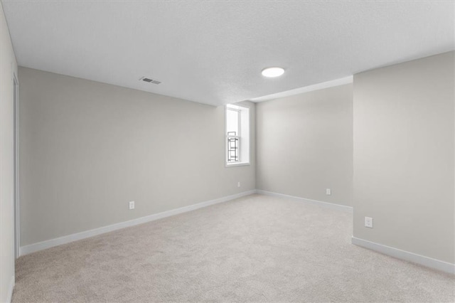 spare room with light carpet, baseboards, visible vents, and a textured ceiling