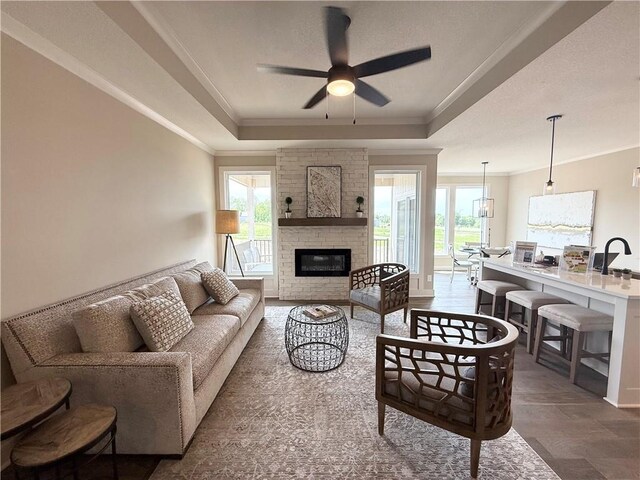 25031 W 94th Ter, Lenexa, KS 66227 - living room featuring a raised ceiling, healthy amount of natural light, ornamental molding, a ceiling fan, and a fireplace