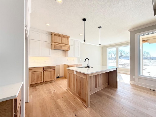 kitchen with pendant lighting, light countertops, white cabinetry, a sink, and an island with sink