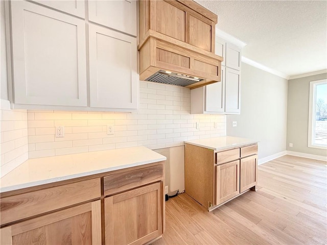 kitchen with light countertops, ornamental molding, light wood-type flooring, and white cabinets