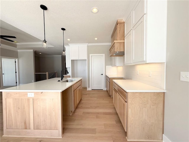 kitchen with light countertops, white cabinets, a sink, and an island with sink