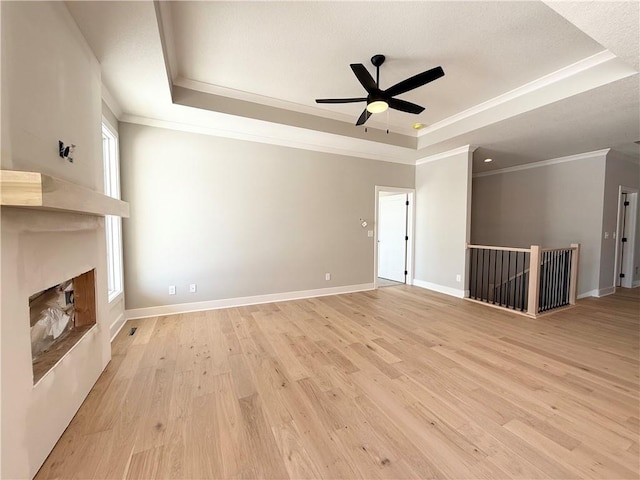 unfurnished living room with light wood finished floors, a large fireplace, baseboards, and a raised ceiling