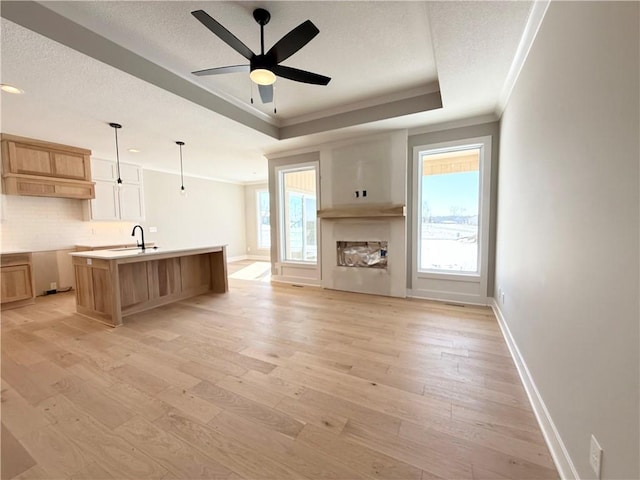 kitchen featuring light countertops, a tray ceiling, light wood finished floors, a center island with sink, and pendant lighting