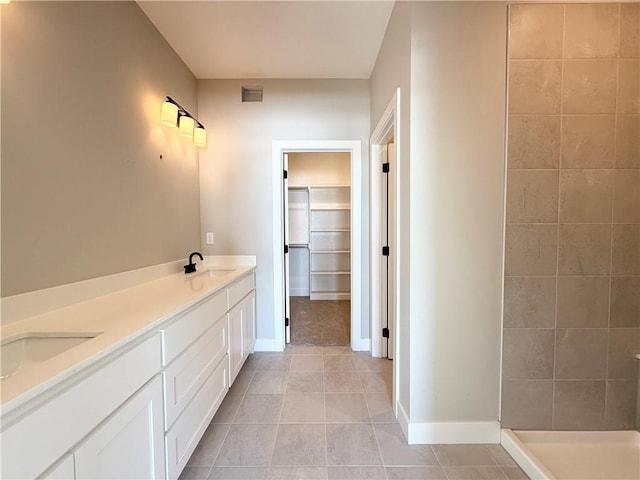 full bath featuring a walk in closet, double vanity, a sink, baseboards, and tile patterned floors