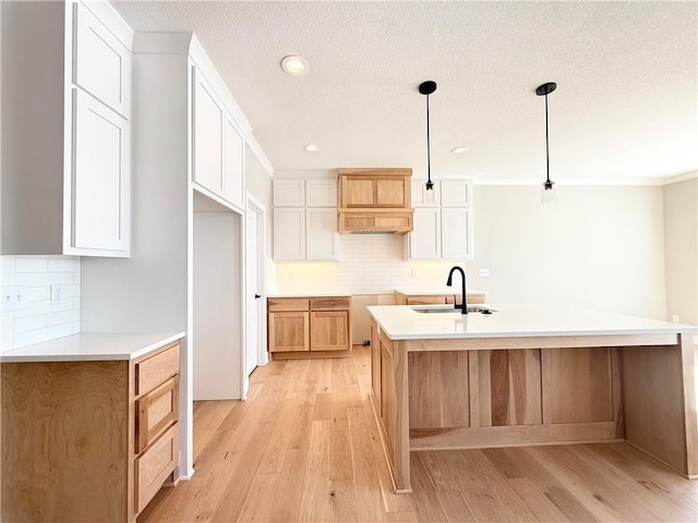 kitchen with light countertops, hanging light fixtures, white cabinets, a sink, and a kitchen island with sink