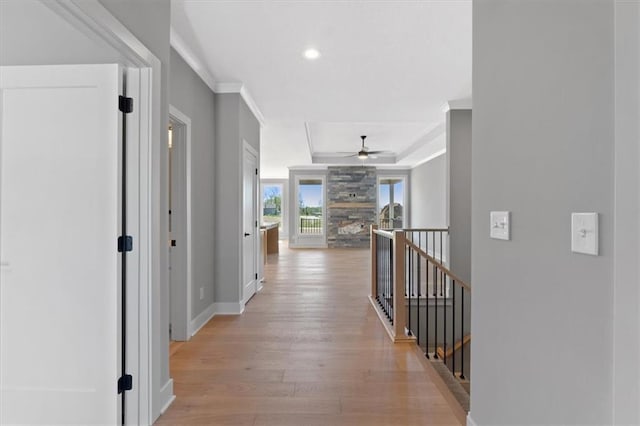 hall with crown molding, baseboards, a raised ceiling, an upstairs landing, and light wood-style flooring