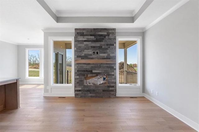 unfurnished living room with crown molding, light wood-style flooring, a wealth of natural light, and a stone fireplace