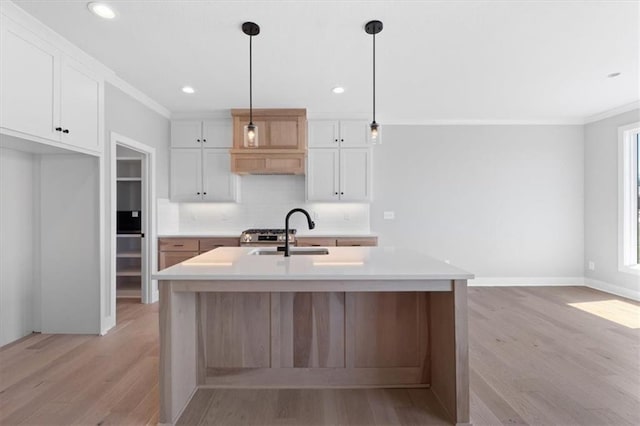 kitchen featuring backsplash, a sink, light countertops, ornamental molding, and light wood-style flooring