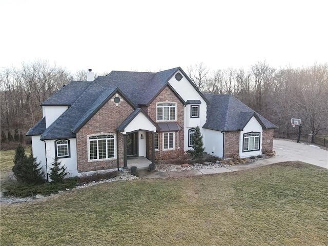 view of front facade featuring brick siding, a chimney, a front yard, and a shingled roof