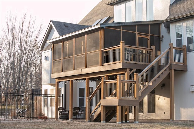 rear view of property with a sunroom, roof with shingles, stairs, fence, and stucco siding