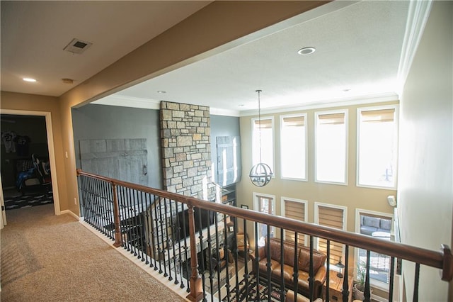 hallway with an upstairs landing, visible vents, baseboards, ornamental molding, and carpet