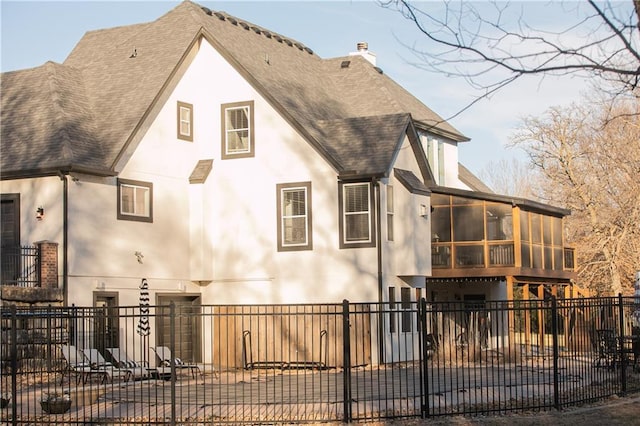 view of front facade featuring a chimney, fence, a sunroom, and stucco siding