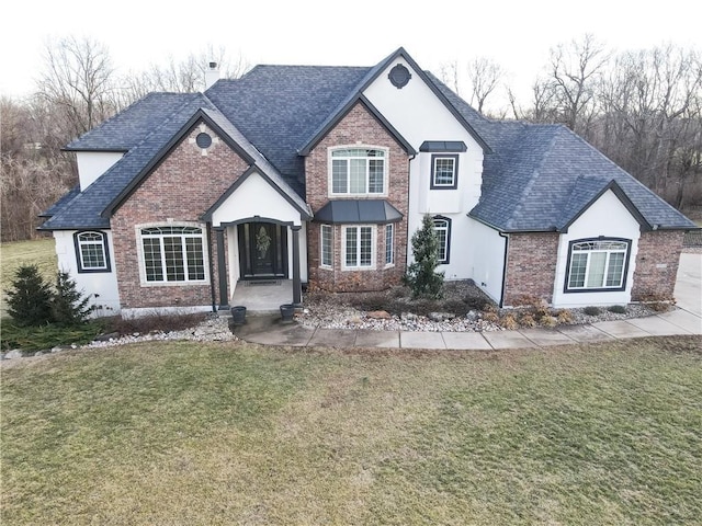 view of front of house with stucco siding, a shingled roof, a front yard, and brick siding