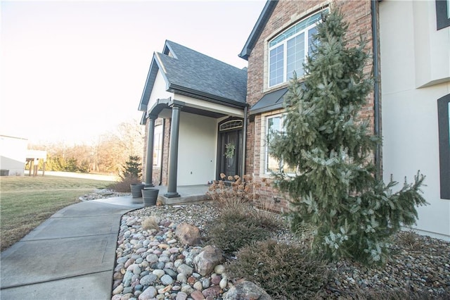 view of side of property with brick siding, a lawn, a shingled roof, and stucco siding