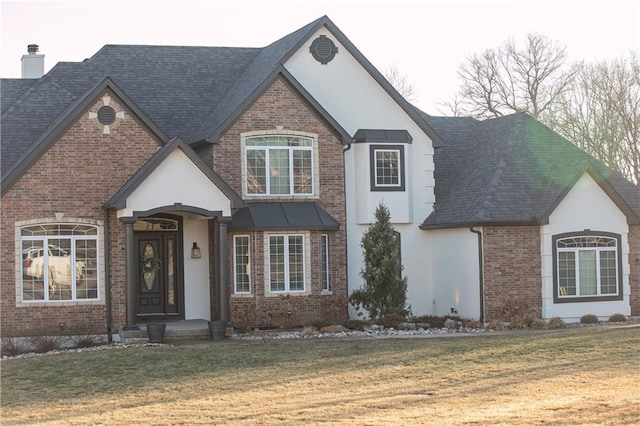 view of front of property with stucco siding, roof with shingles, a front yard, and brick siding
