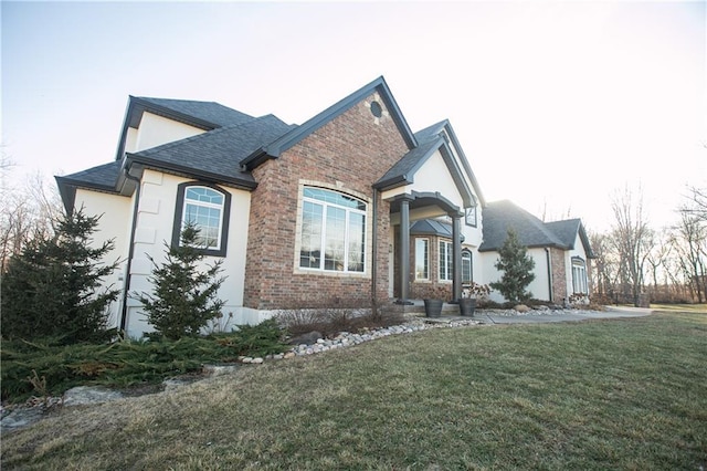 view of front of property featuring a front lawn, roof with shingles, brick siding, and stucco siding